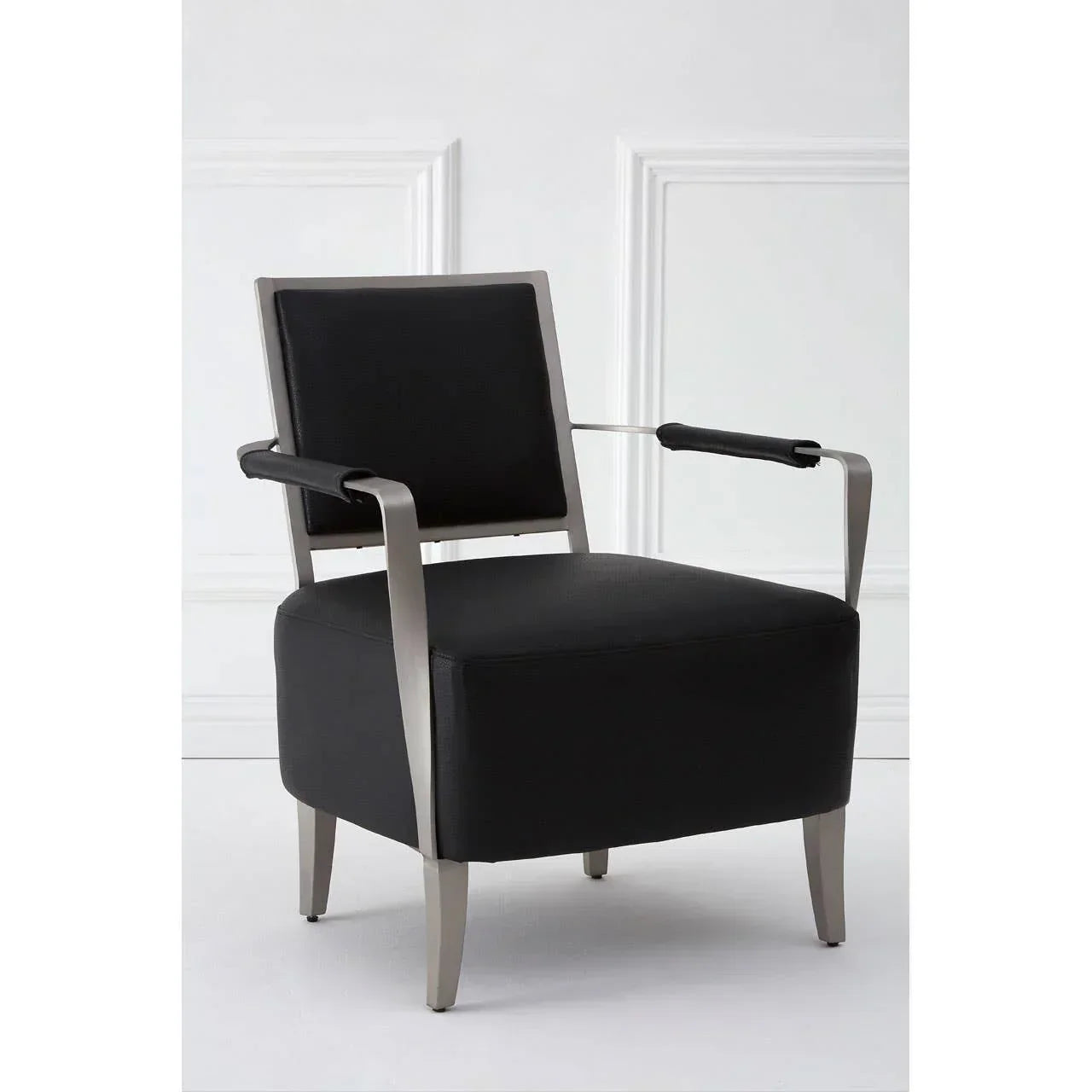Black leather accent chair with metal frame and padded armrests against white panel wall