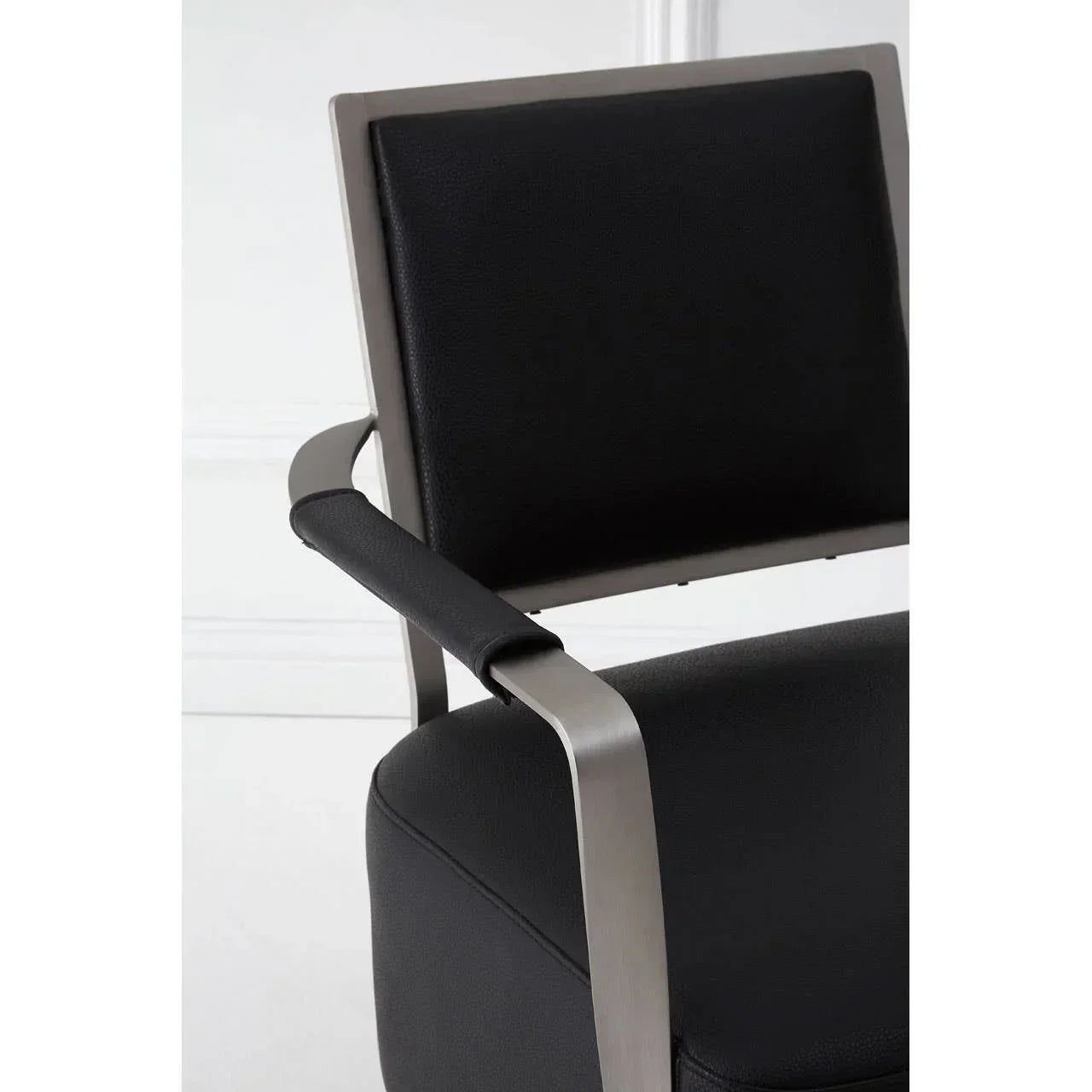 Black faux leather dining chair with brushed metal arm and cushioned backrest close-up