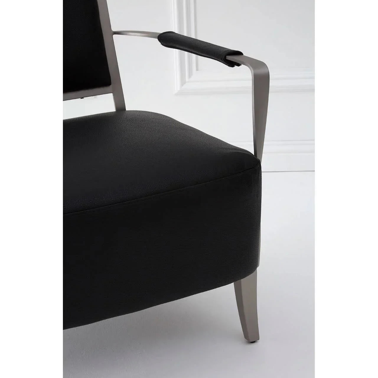 Black leather armchair with brushed metal legs and padded armrest in modern setting