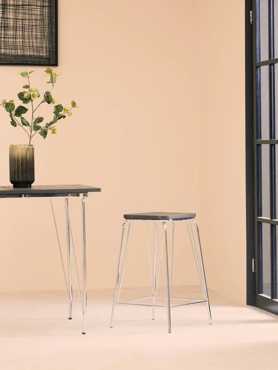 Modern bar stool with chrome legs and black seat next to matching table in bright room