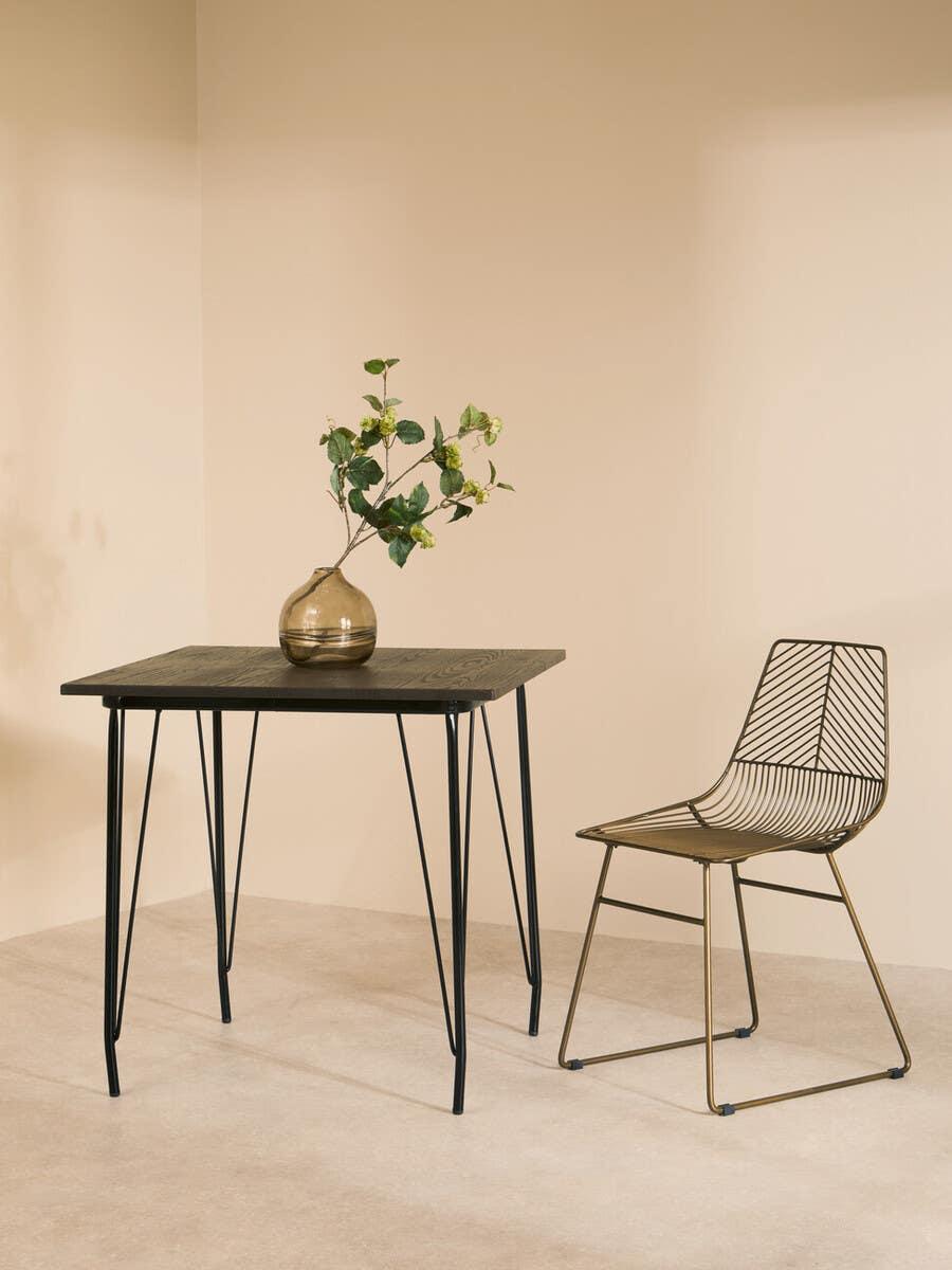 Modern dining table with black metal legs and wire chair, glass vase with greenery on top