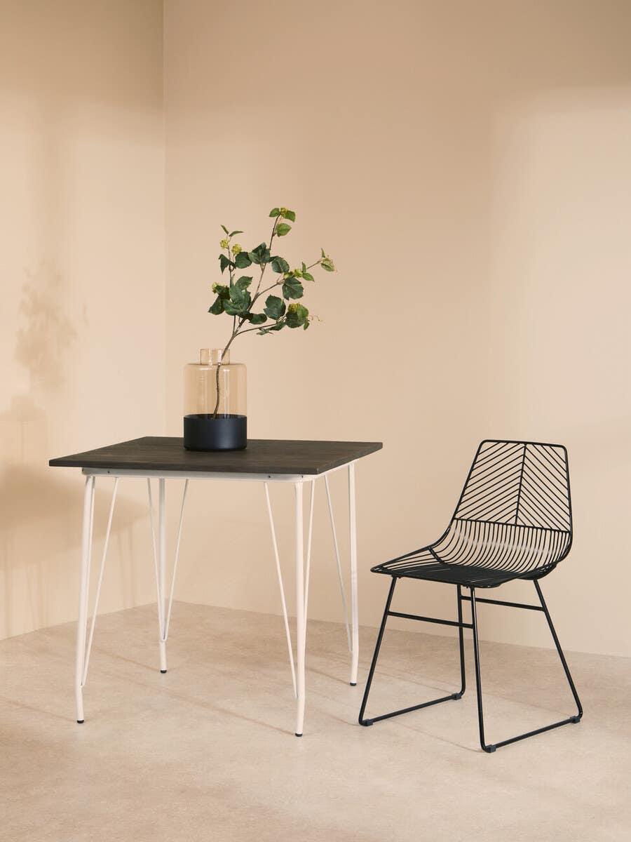 black wire dining chair beside square table with white legs and vase in minimalist room