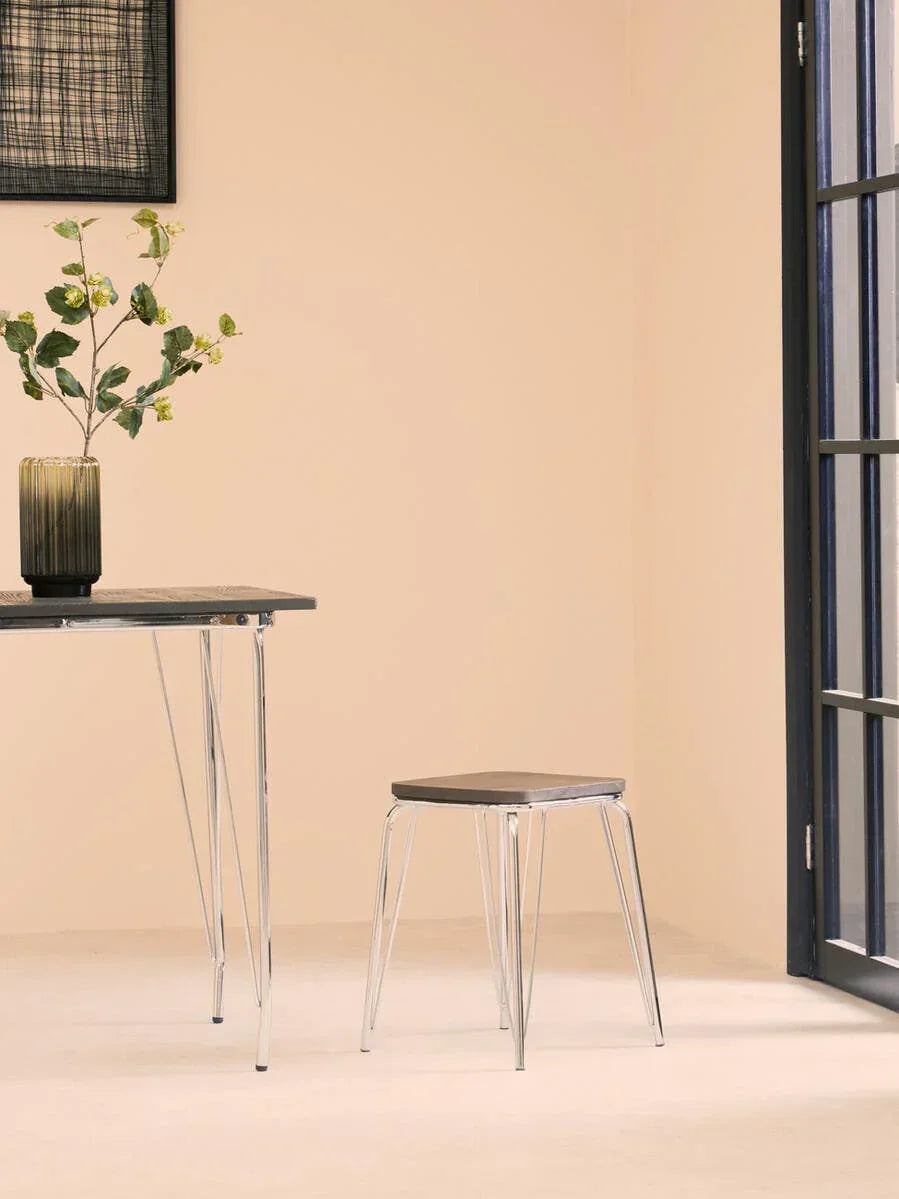 Modern dining stool with black seat and chrome legs beside table in minimalistic room
