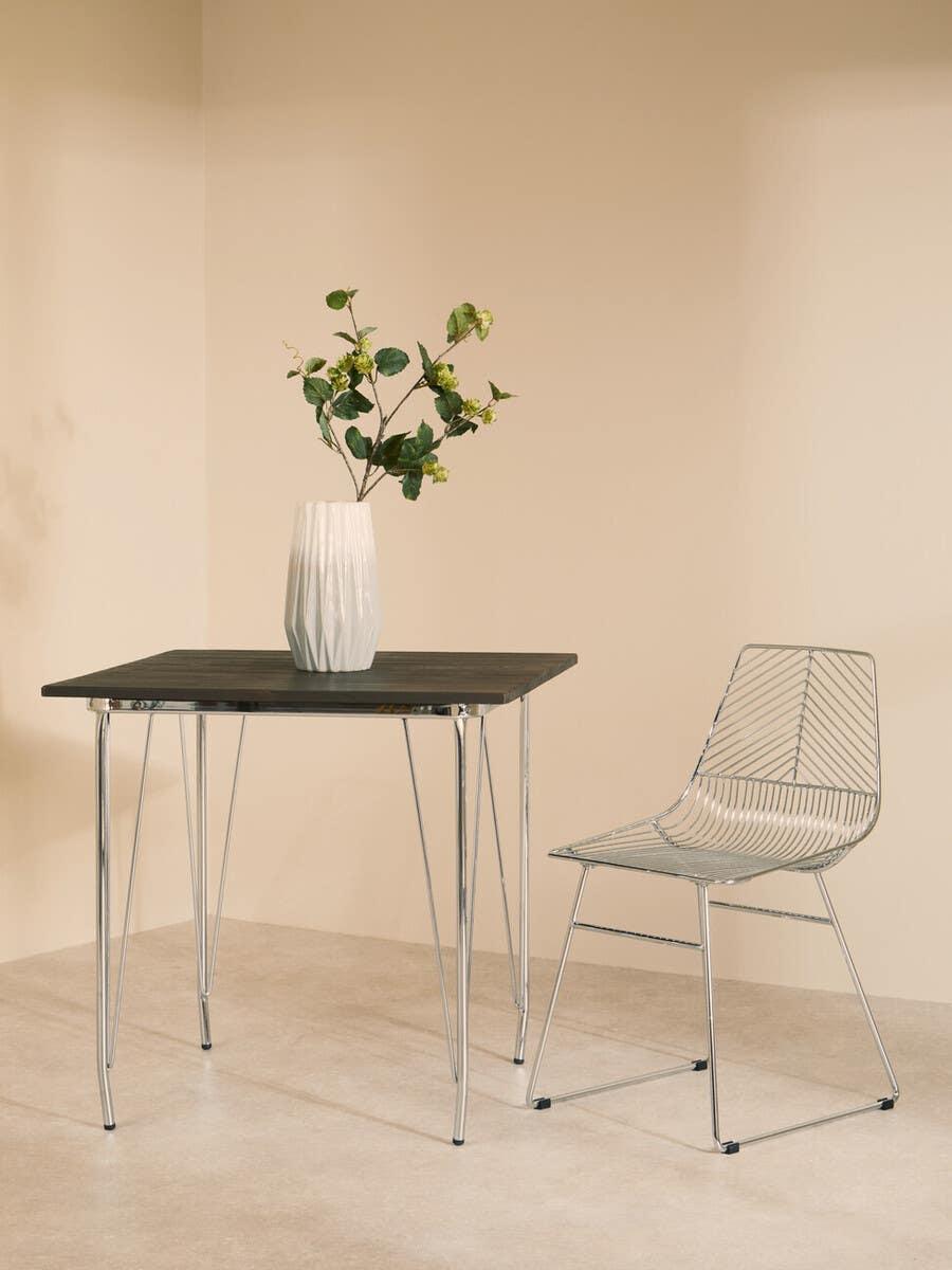 Modern metal dining chair beside square dark wood table with white vase and green plant
