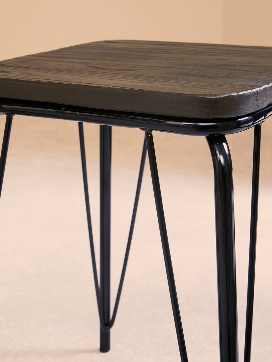 Small stool featuring a square black metal frame with slender legs and a smooth elm wood seat, set against a neutral background