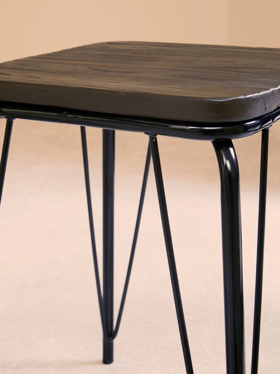 Small stool featuring a square black metal frame with slender legs and a smooth elm wood seat, set against a neutral background