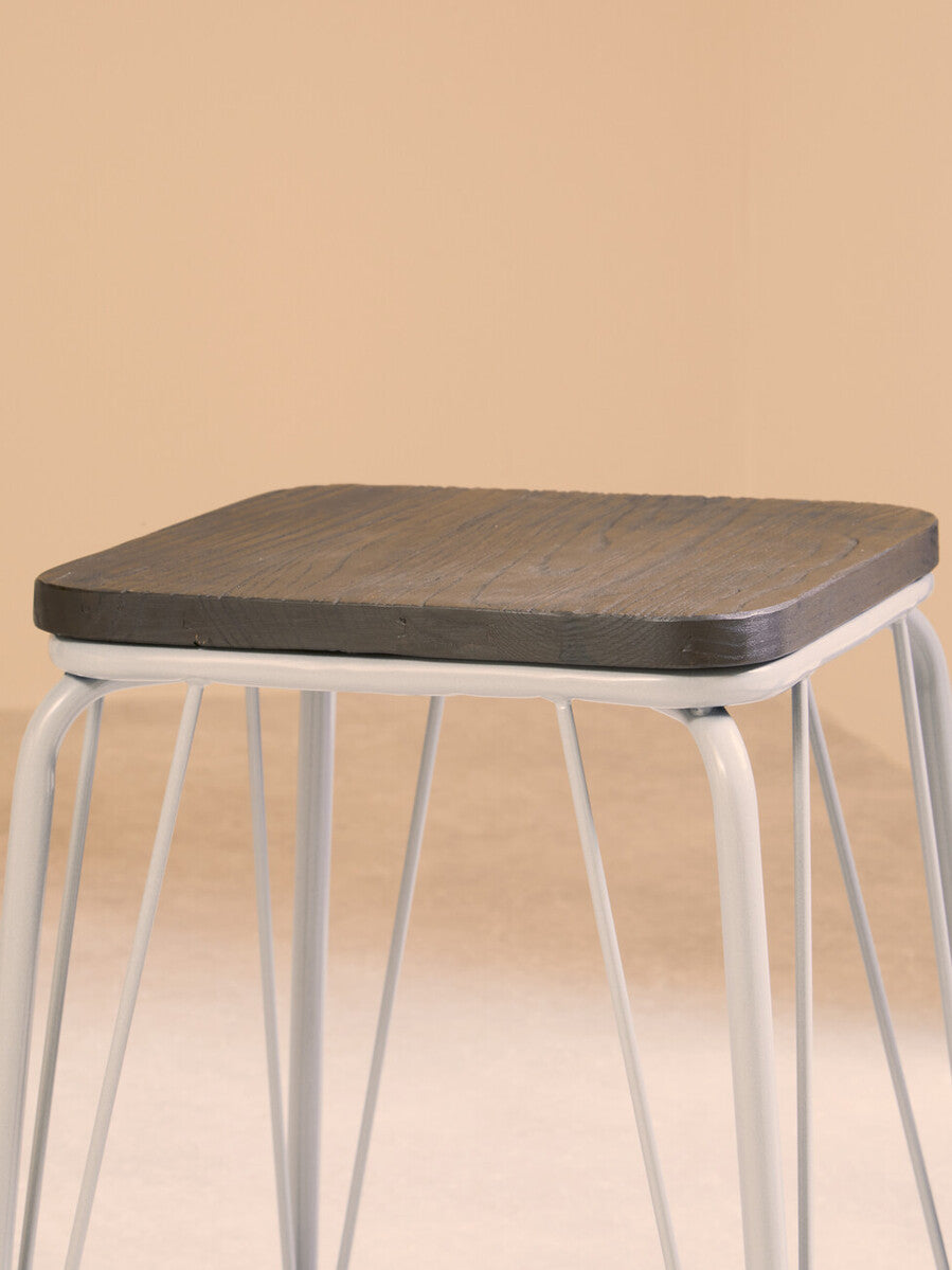 Small stool featuring a grey metal frame and a dark elm wood seat, with slender legs providing a modern and minimalist design. The background is a soft, neutral color that complements the stool's aesthetic