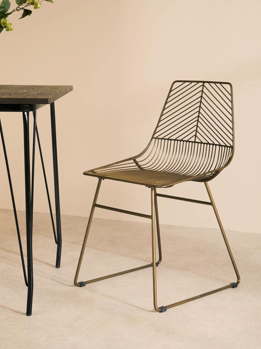 Metal dining chair with geometric wire design beside black leg table on light floor