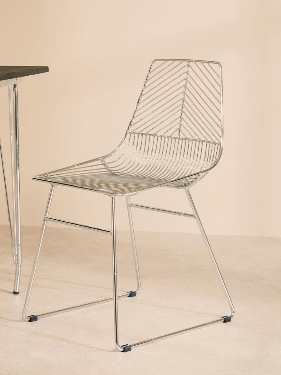 Modern chrome dining chair with wire frame next to table on light tile floor