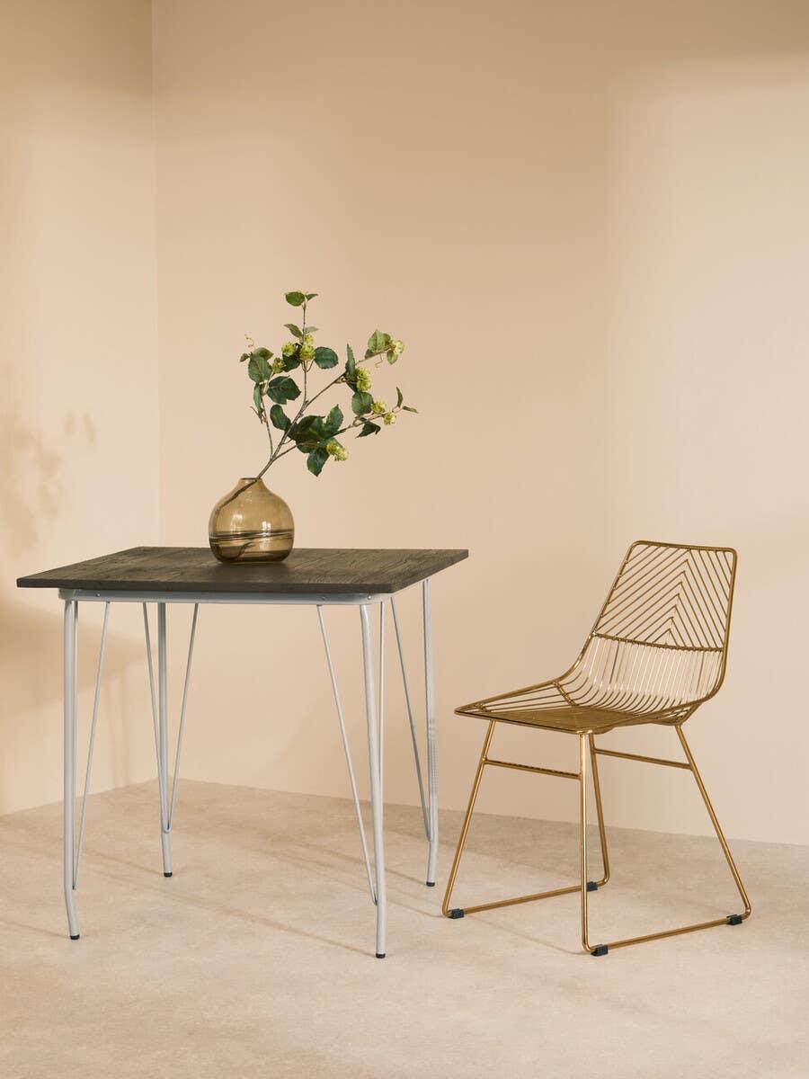 Modern dining table with black wood top and metal legs beside gold wire dining chair