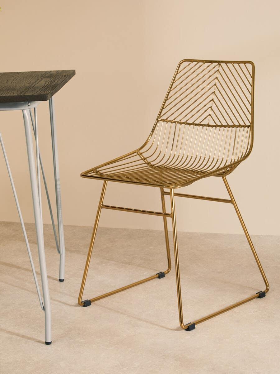 Gold metal dining chair with geometric wire design beside black wood table