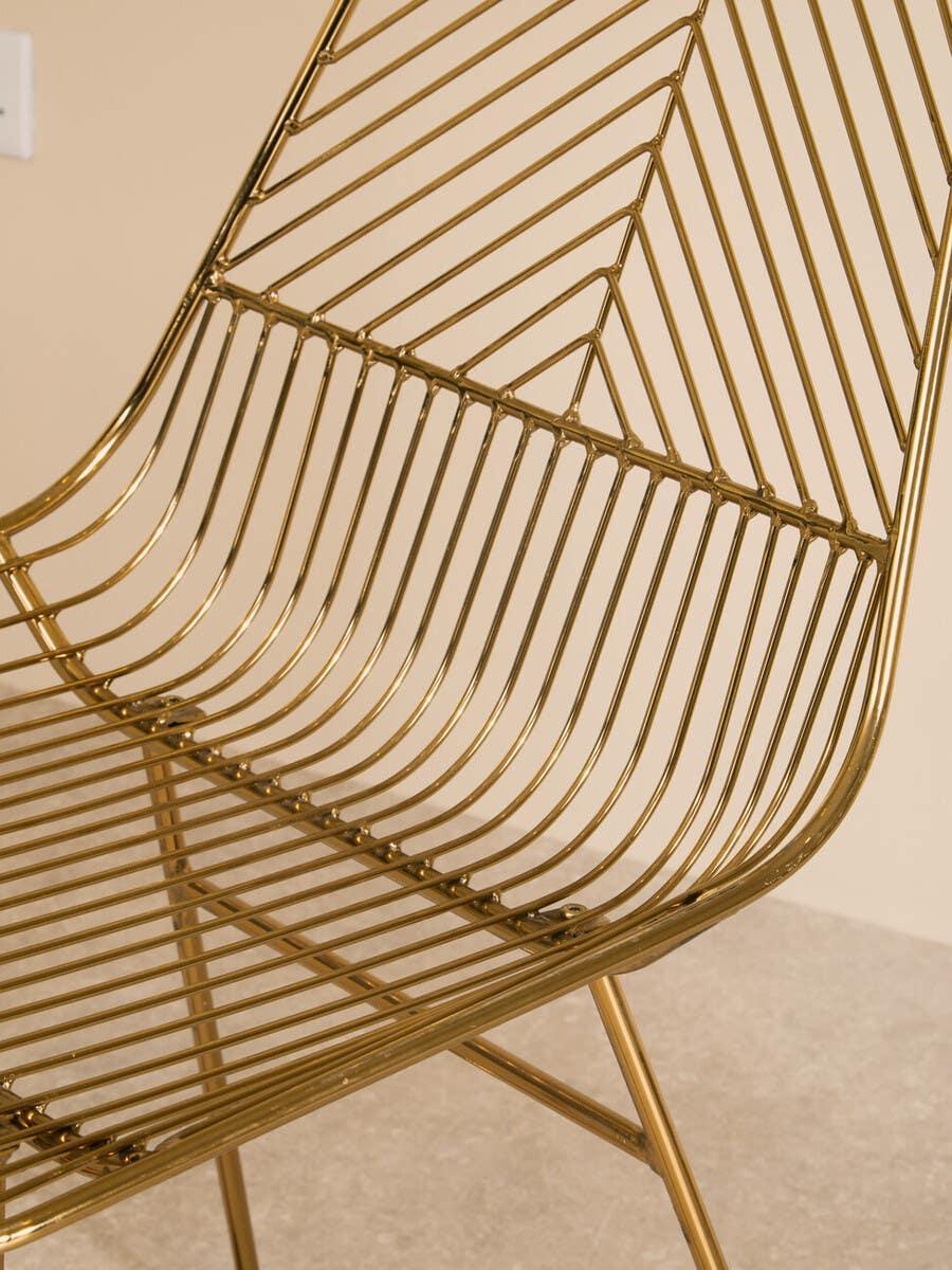 Gold metal dining chair with geometric wire design and angled legs on beige floor
