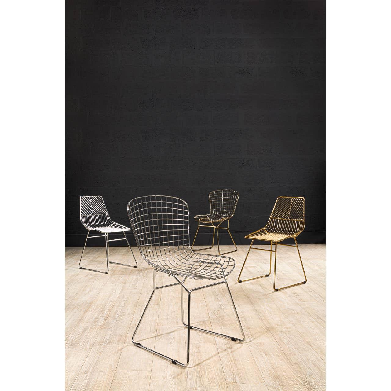 Metal wire dining chairs in chrome and gold finishes on light wood floor against dark wall