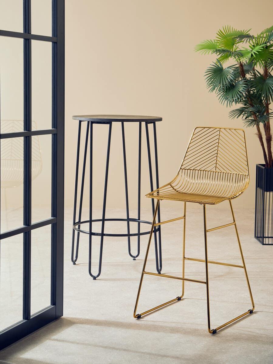 Gold metal bar stool with wire frame beside black high round table in modern room