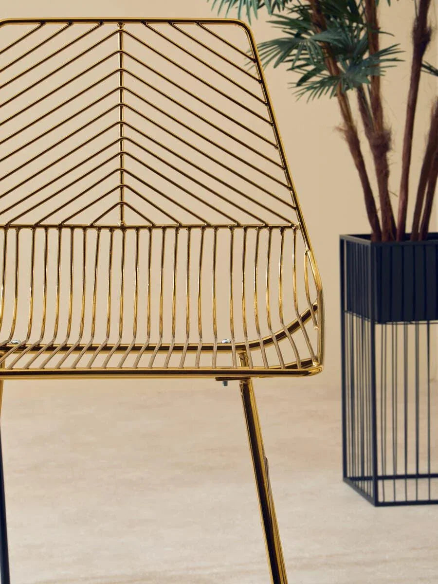 Gold metal accent chair with geometric wire backrest beside tall indoor plant