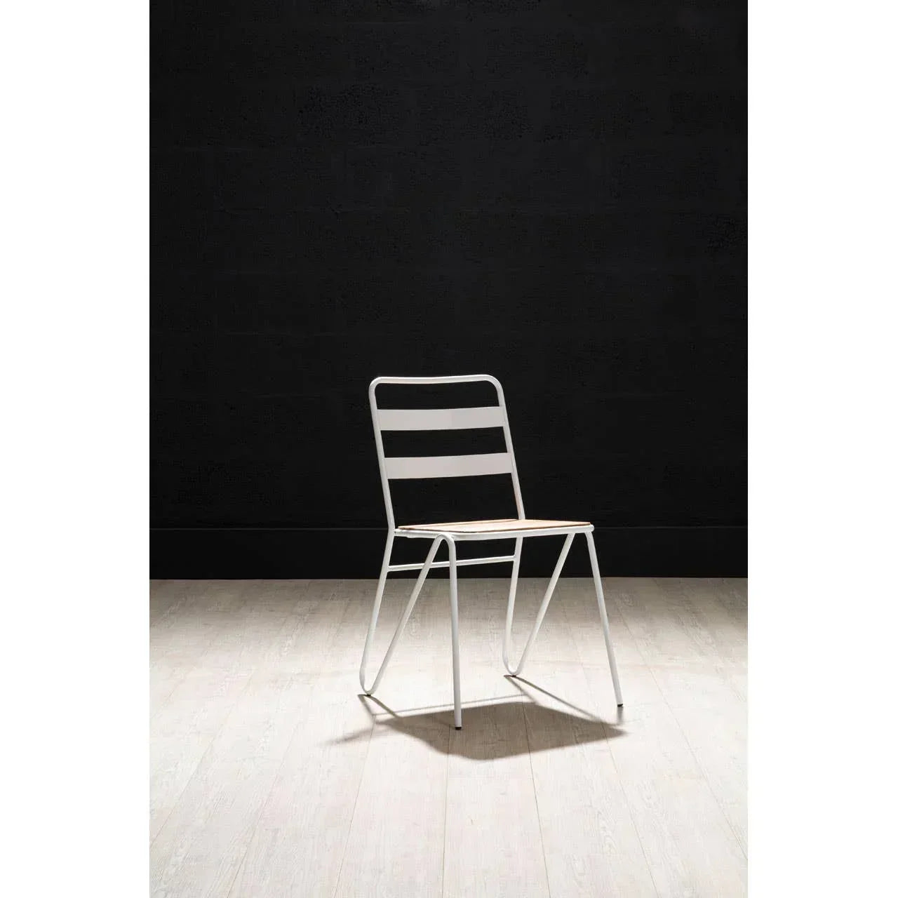 White metal dining chair with slatted backrest on light wood floor against dark wall