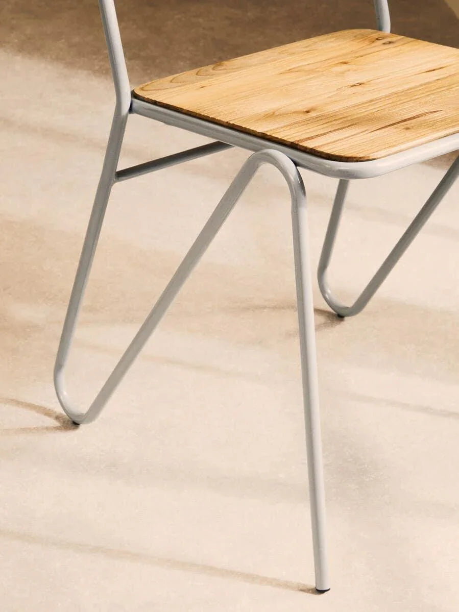 Close view of dining chair with natural wood seat and white metal legs on beige floor