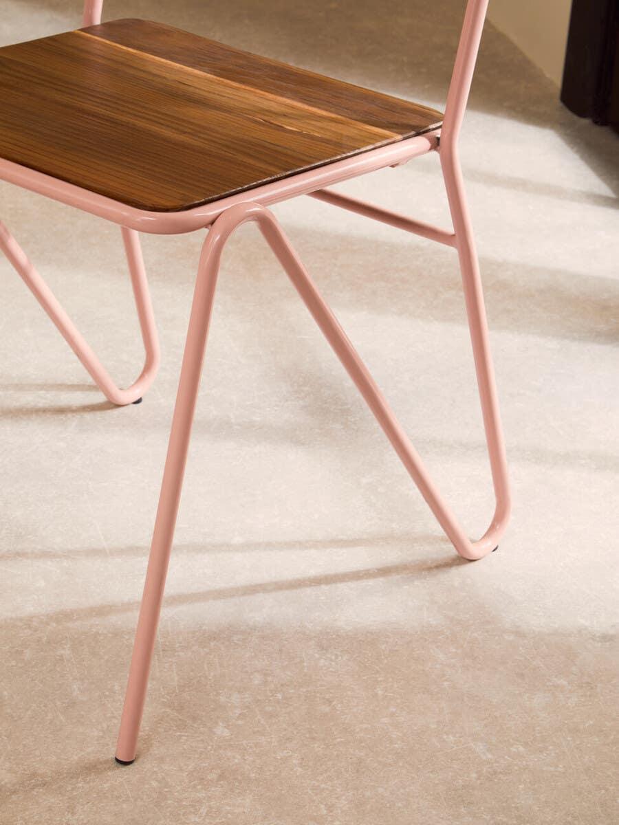 Modern dining chair with pink metal legs and wood seat on stone tile floor