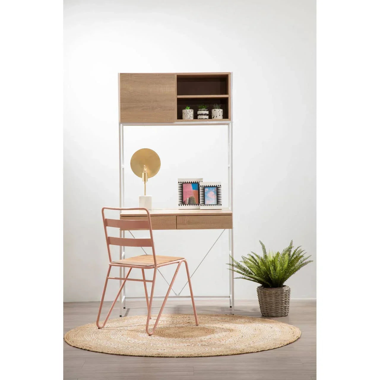 Modern wooden desk with shelving, pink metal chair, table lamp and plant on round rug