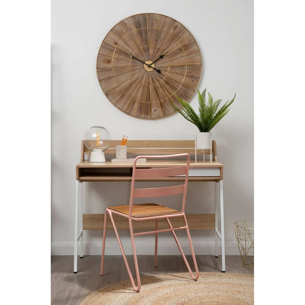 Wooden desk with white metal legs, pink chair, lamp, plant and large wooden wall clock