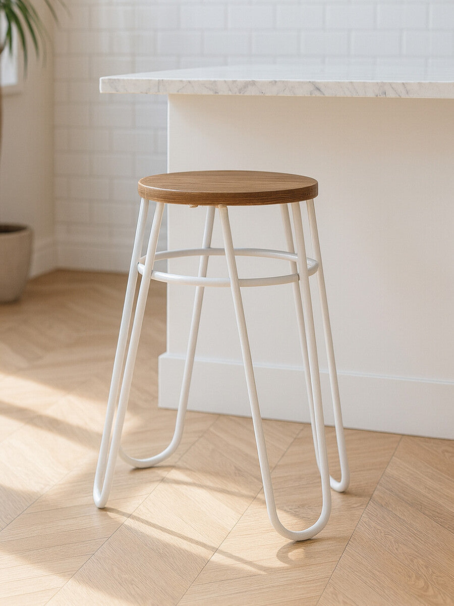 A grey metal hairpin stool with a round wooden seat, featuring a minimalist design and slender legs, placed on a light wooden floor in a bright, airy room