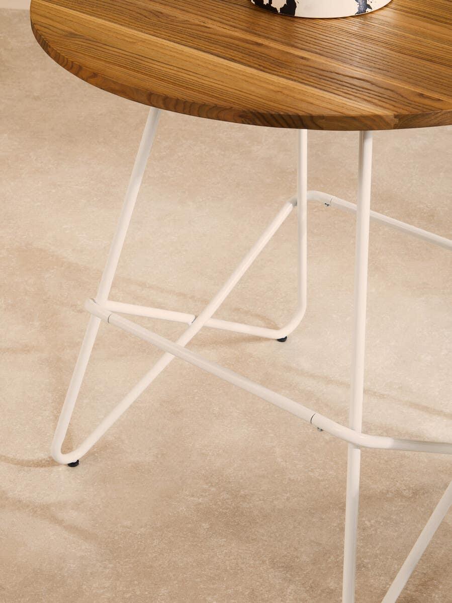 Round wooden side table with white metal legs on beige floor