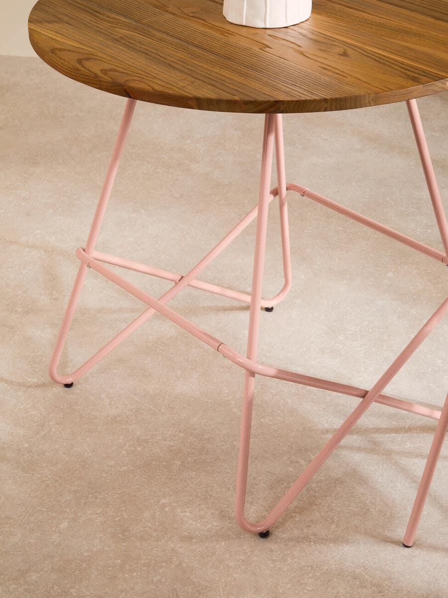 Round wood side table with pink metal legs on beige floor