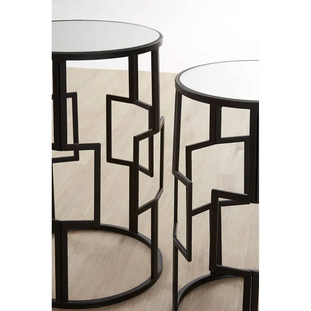 Round metal side tables with geometric black frames and mirrored tops on wooden floor
