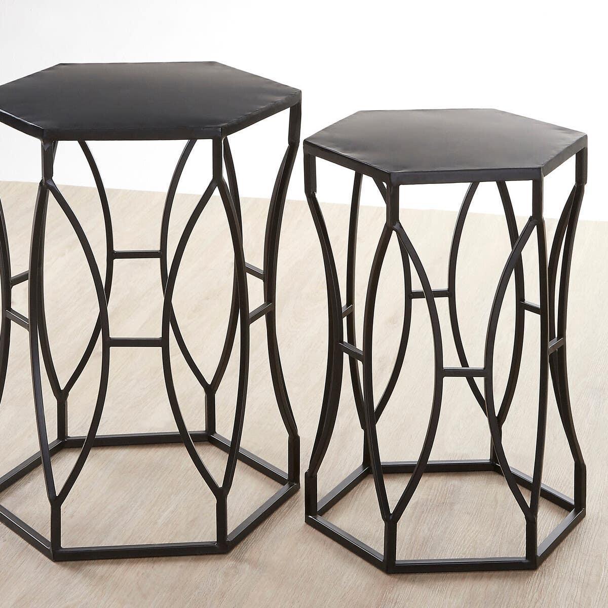 Set of two black metal hexagonal side tables with geometric openwork bases on wood floor