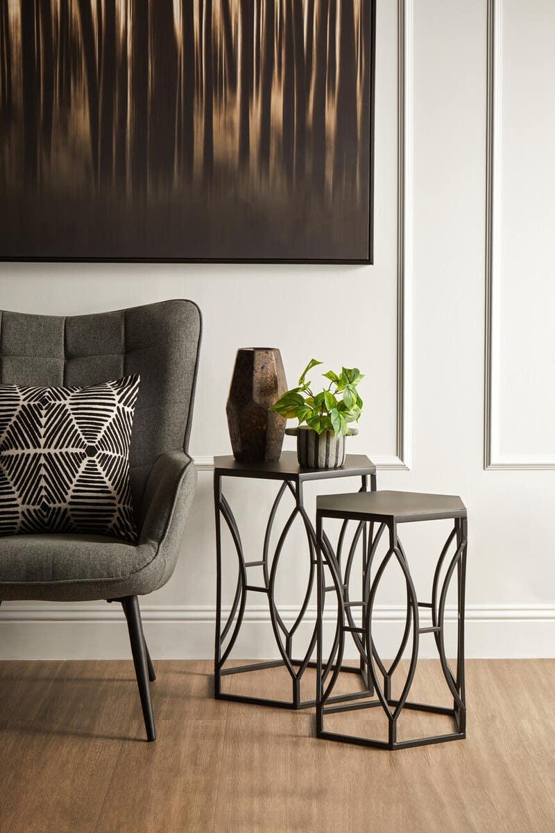 Set of two black metal nesting tables with geometric frames beside grey accent chair