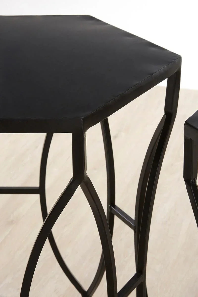 Hexagonal black metal side table with decorative curved legs on light wood floor