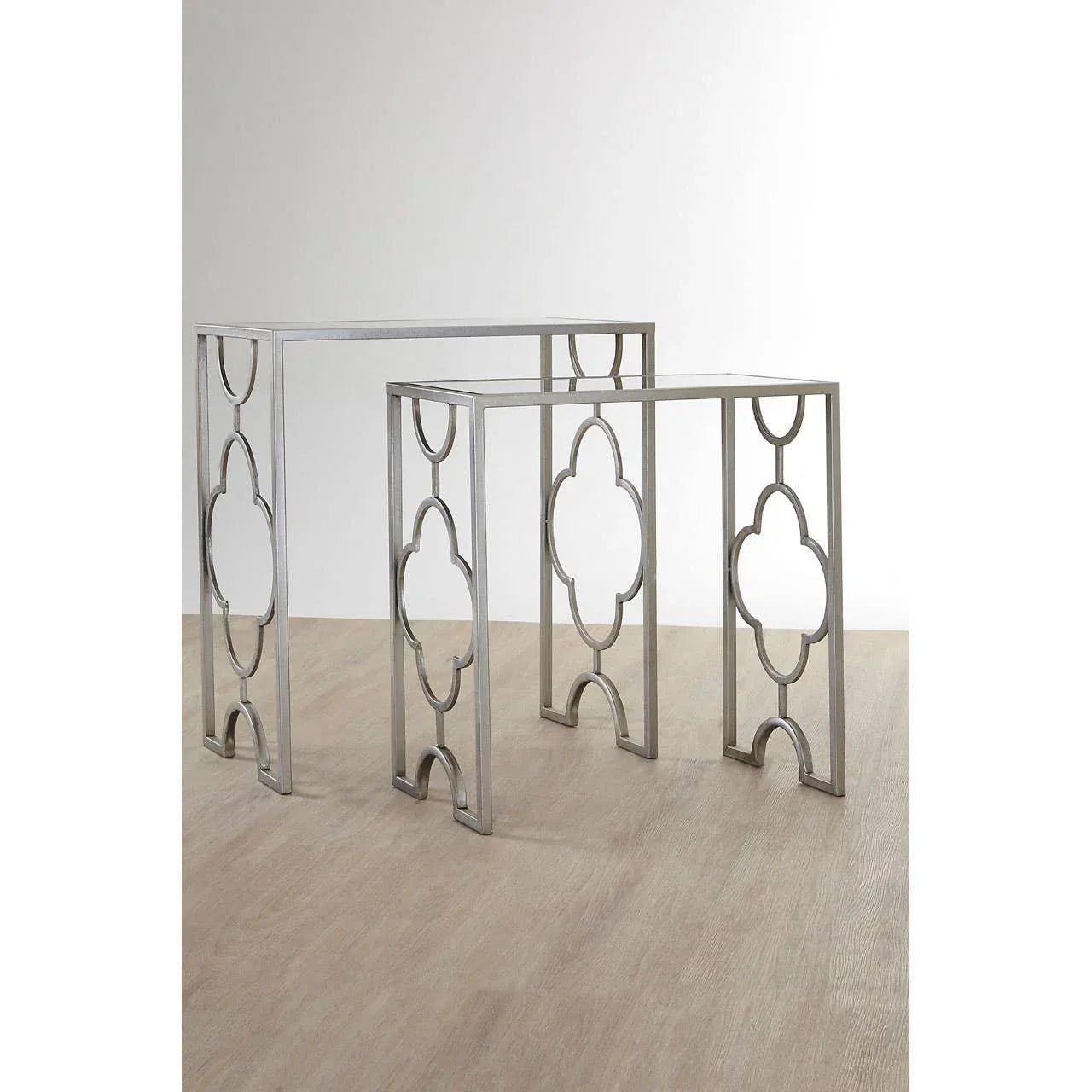 Set of two metal nesting tables with geometric cutout legs on light wood floor