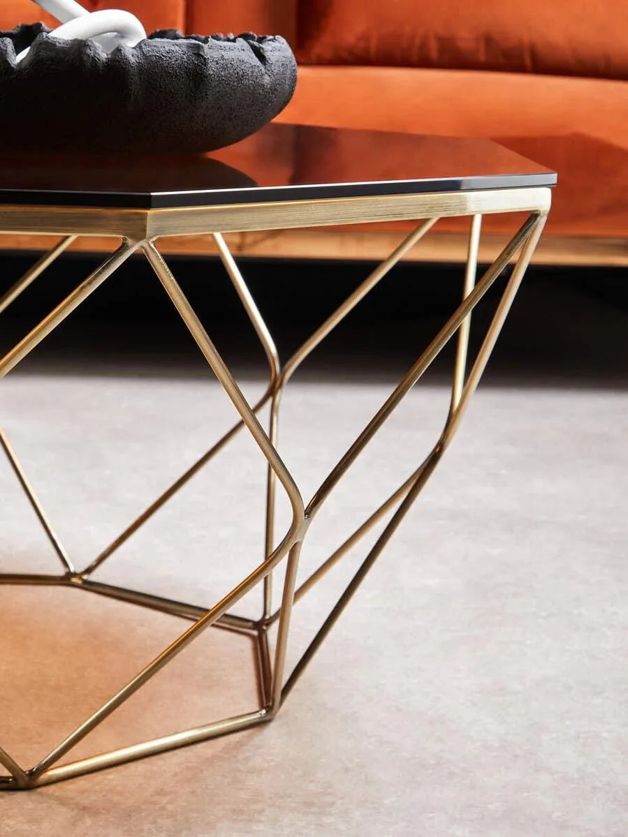 Geometric gold metal coffee table with glass top and decorative bowl in modern living room