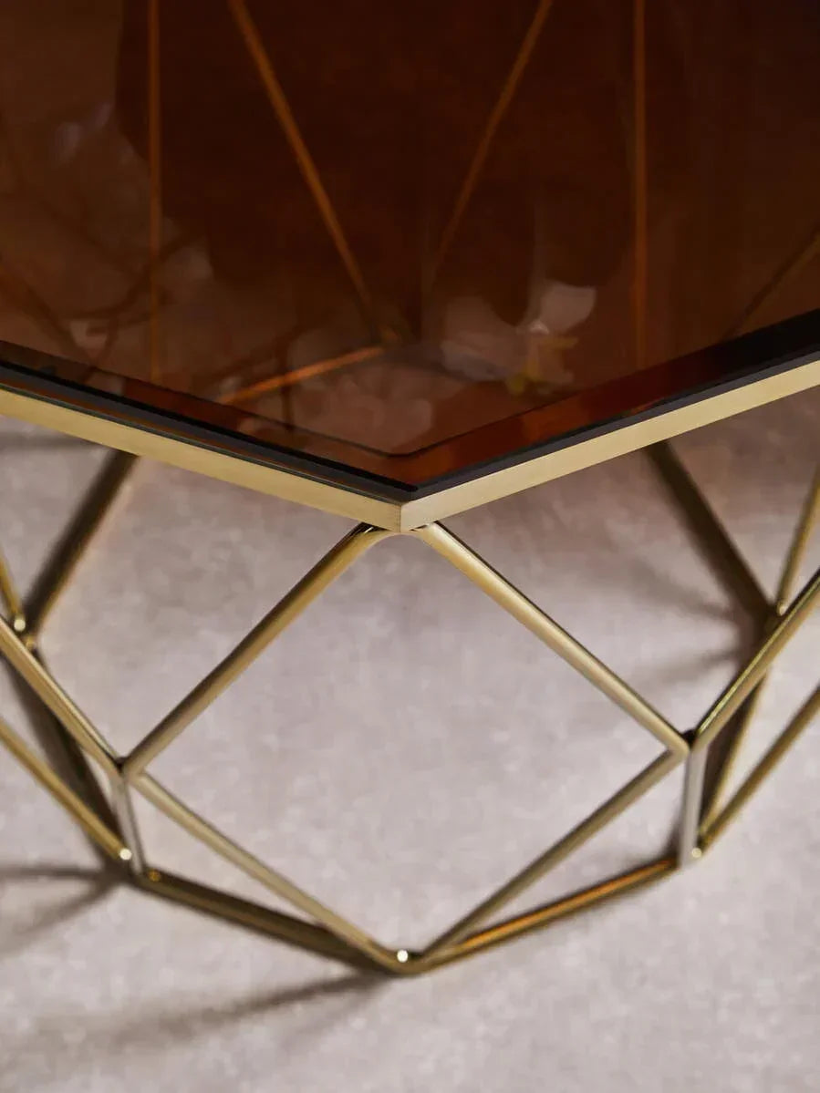 Geometric gold metal coffee table base with brown glass top on carpet