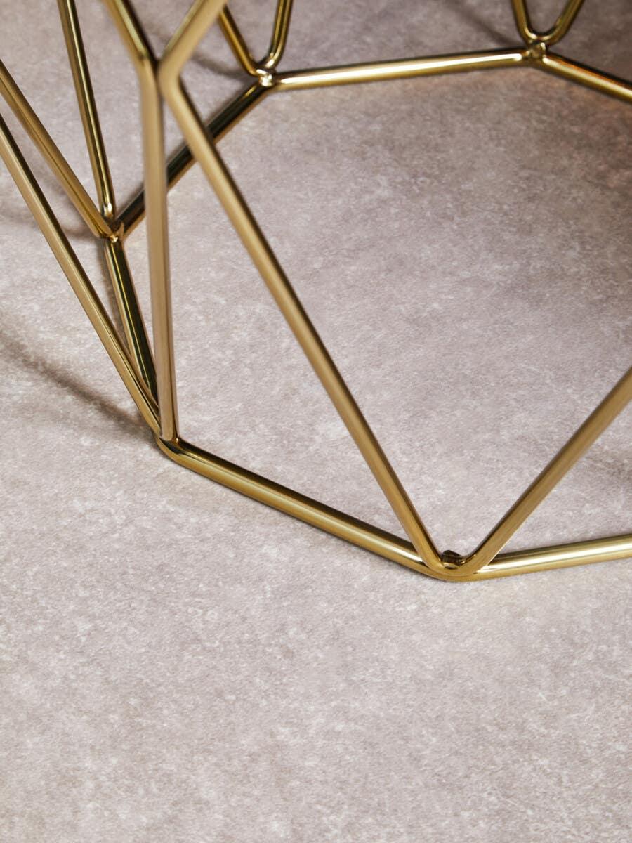 Geometric gold metal coffee table base on light stone floor