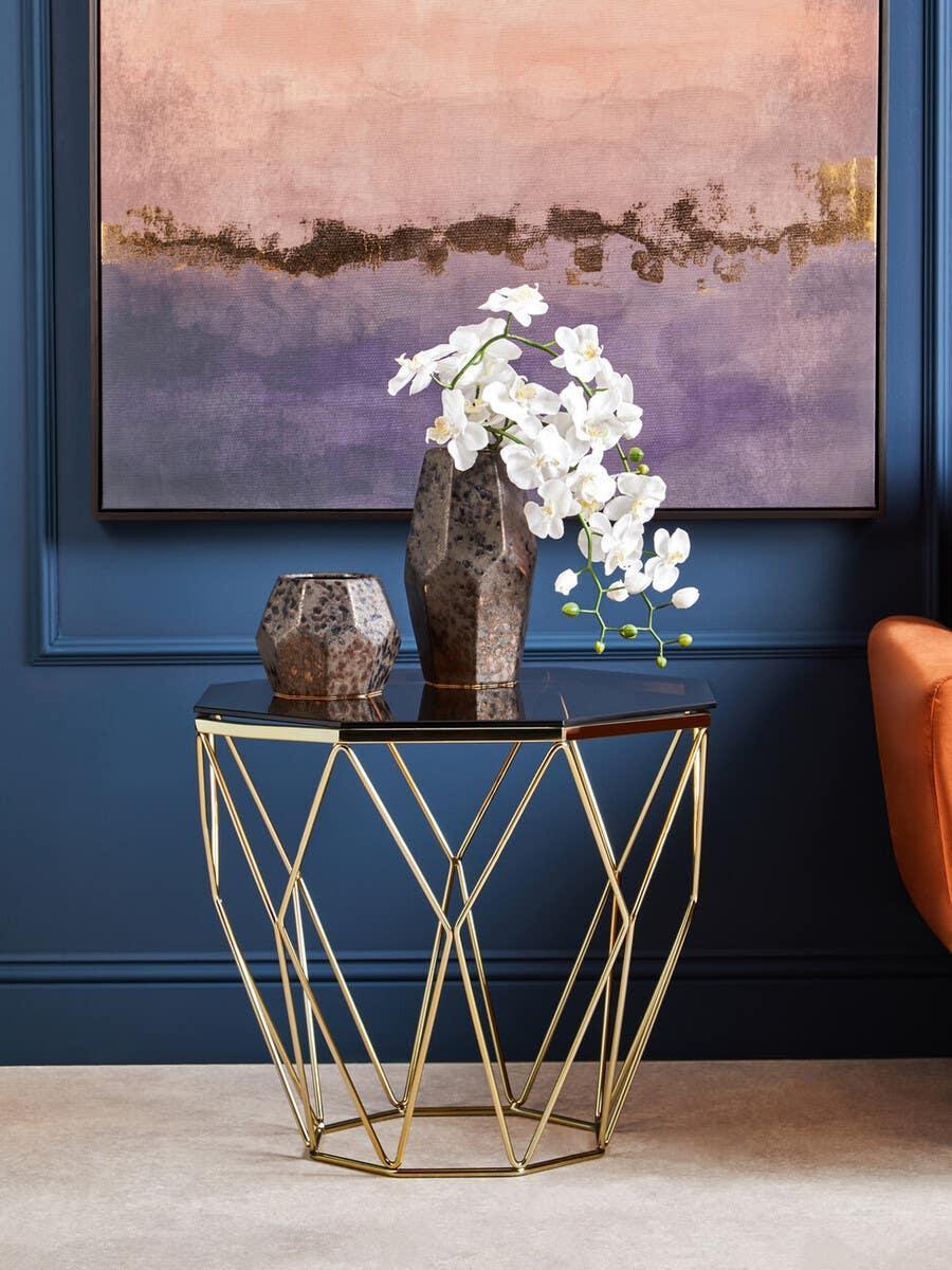 Gold geometric side table with black glass top, decorative vases, and white flowers