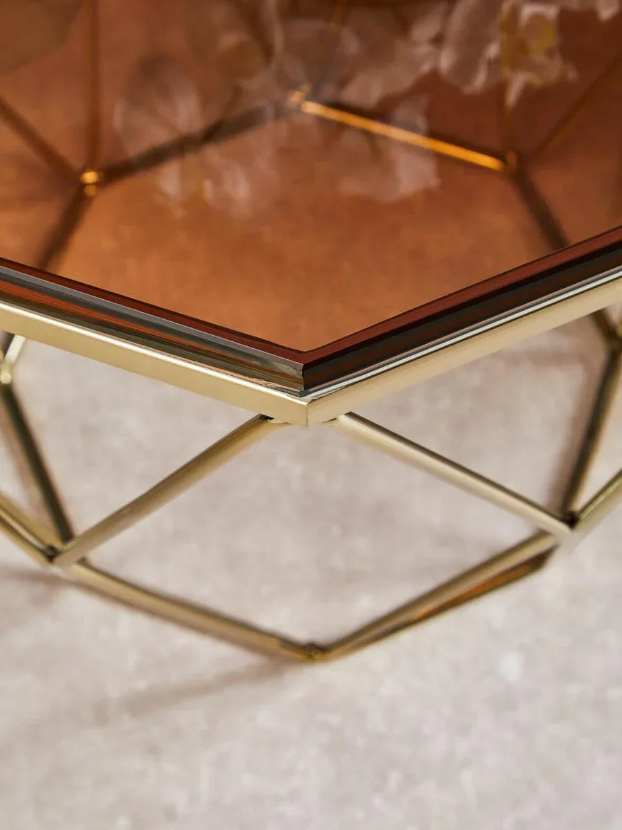 Geometric coffee table with gold metal frame and glass top on light textured flooring