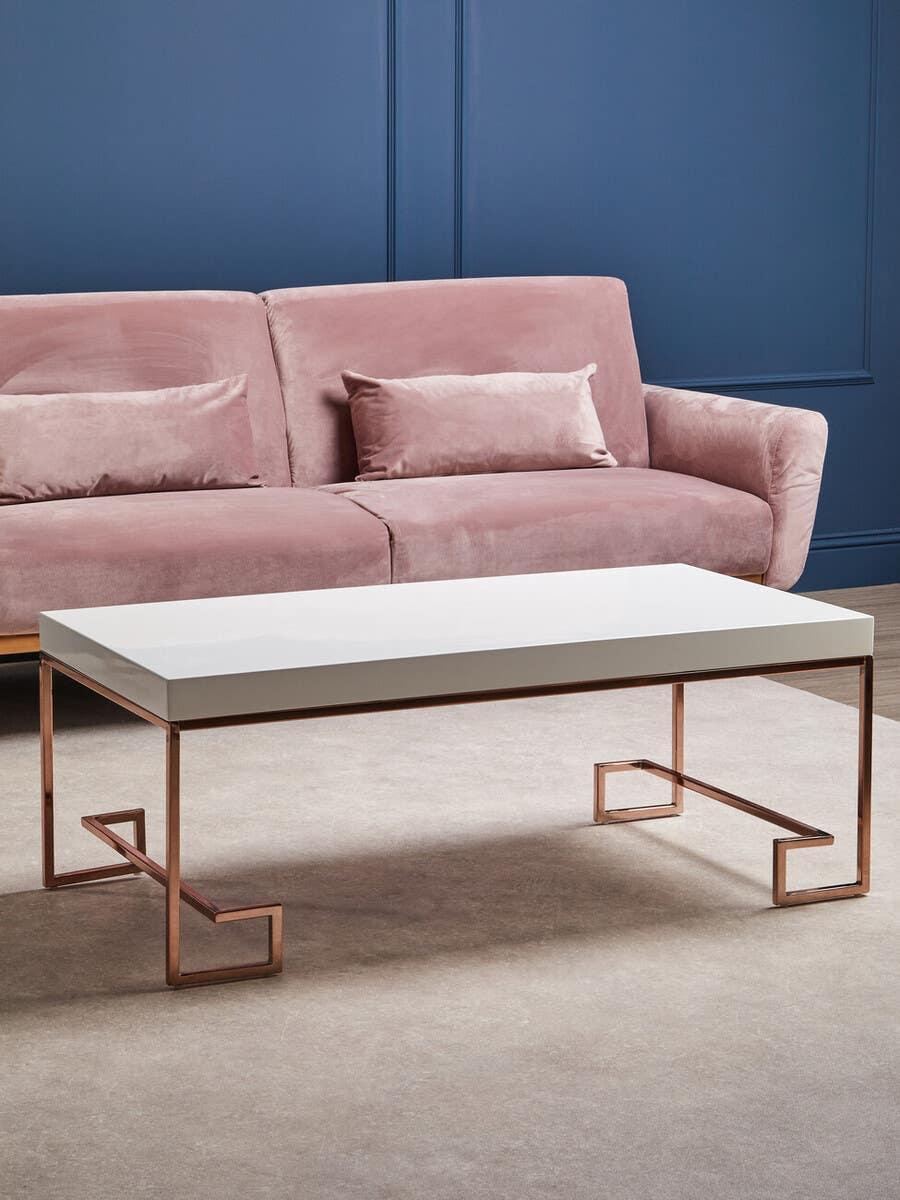 White coffee table with rose gold metal legs in front of a pink velvet sofa