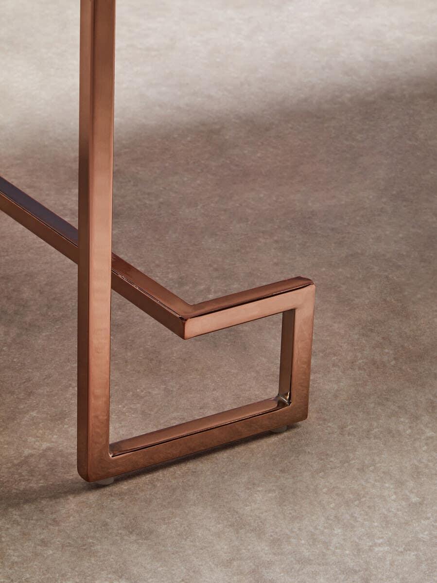 Close-up of copper metal table leg with geometric base on carpeted floor