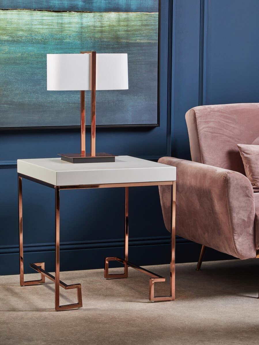Modern side table with rose gold metal legs and white top beside mauve velvet armchair