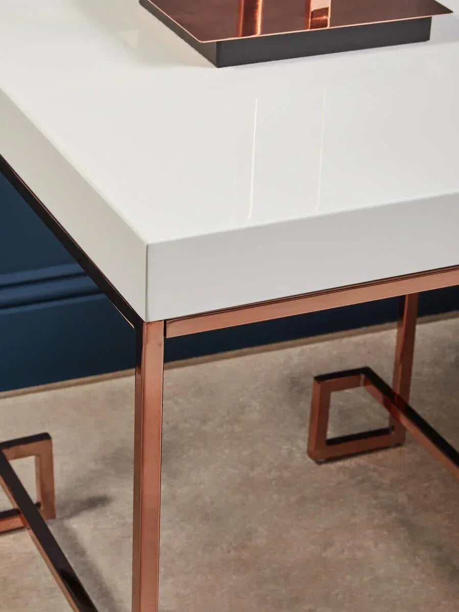 Modern side table with white high gloss top and rose gold metal legs on carpeted floor