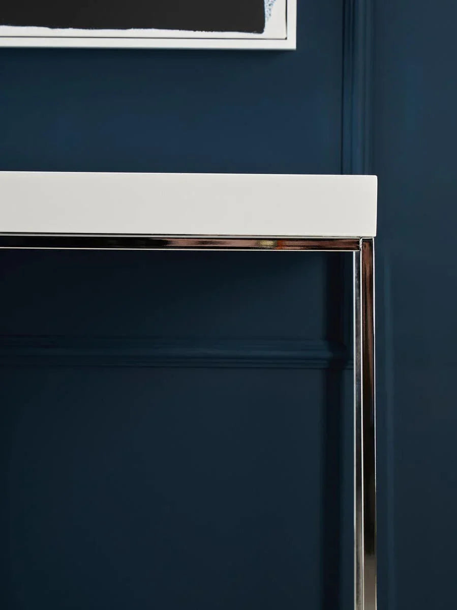 White console table with chrome legs against dark blue paneled wall