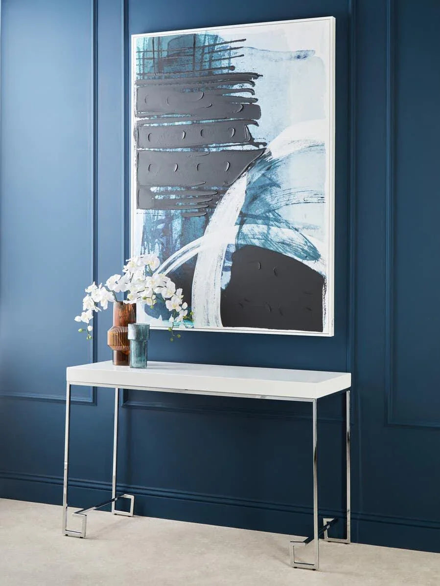 White console table with chrome legs against blue wall, modern vases and abstract artwork