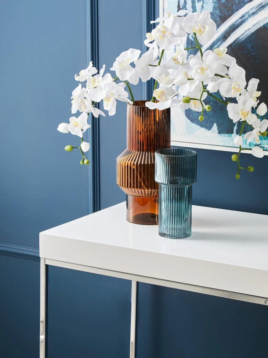 White console table with fluted glass vases and artificial orchid flowers against blue wall