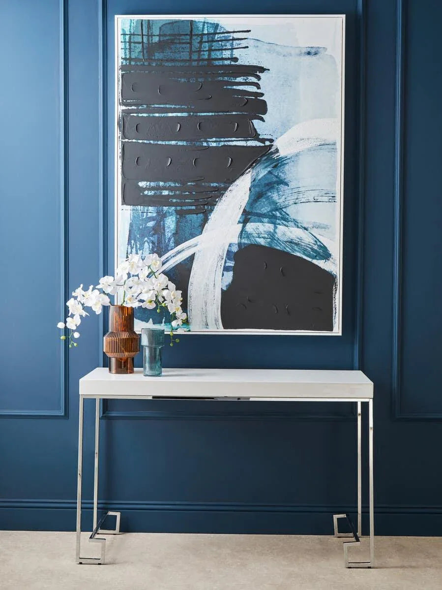 Modern white console table with chrome legs against blue wall, glass vases and orchid flowers