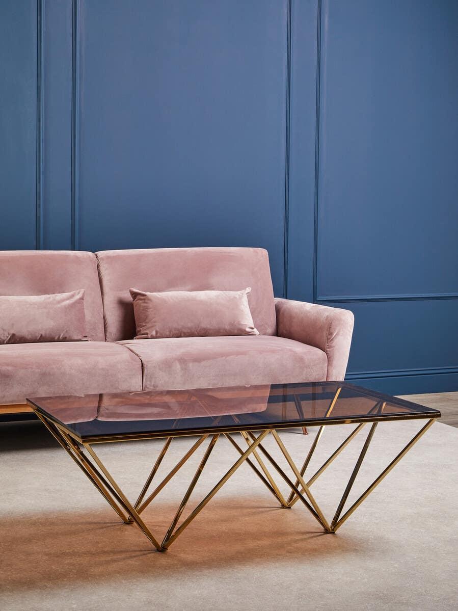Glass top coffee table with gold geometric metal base in front of pink velvet sofa