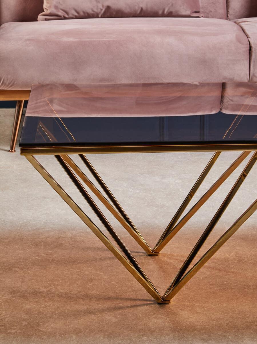Glass coffee table with gold geometric metal base in front of blush velvet sofa
