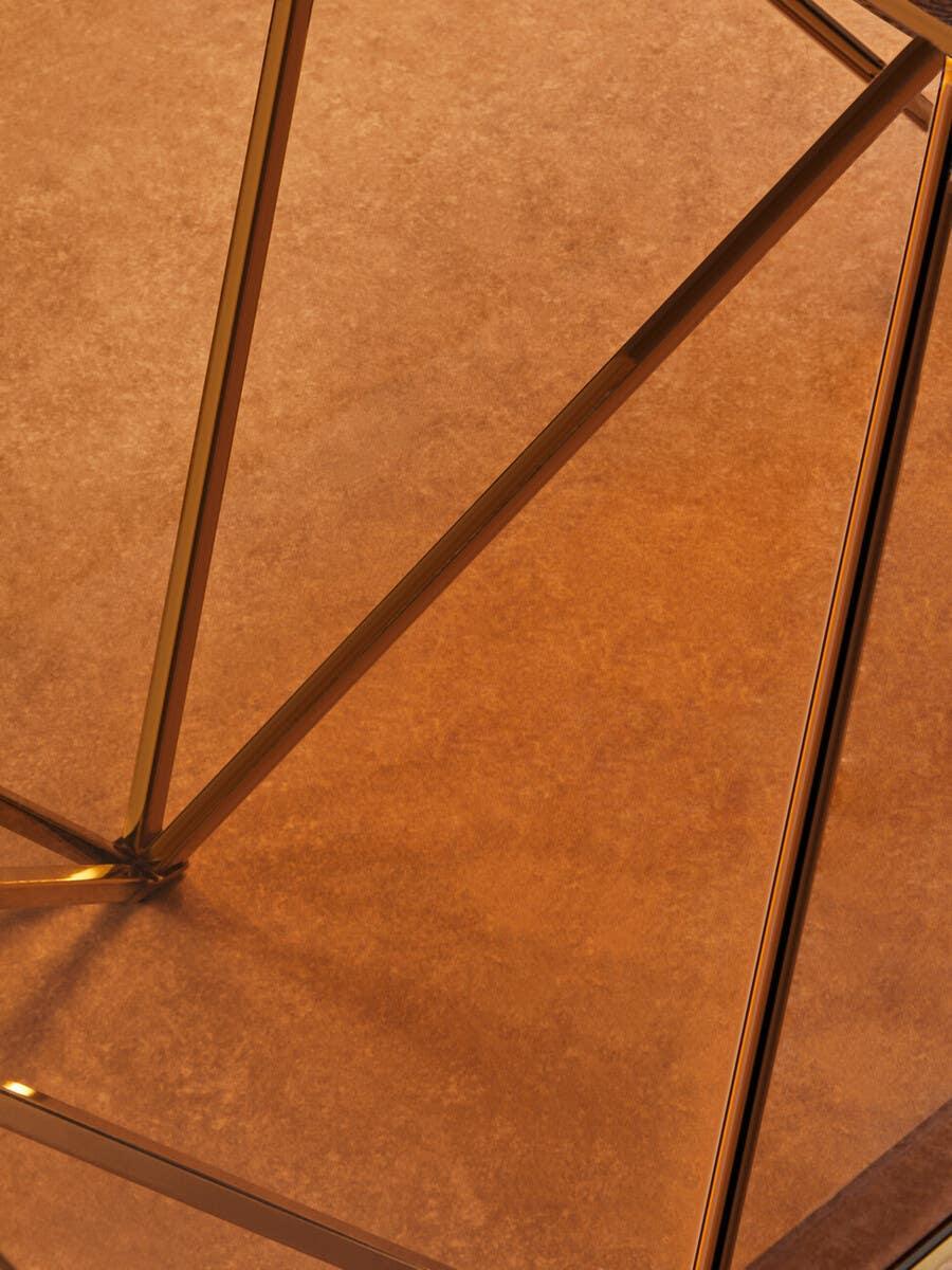 Close-up of geometric gold metal coffee table frame on warm brown surface