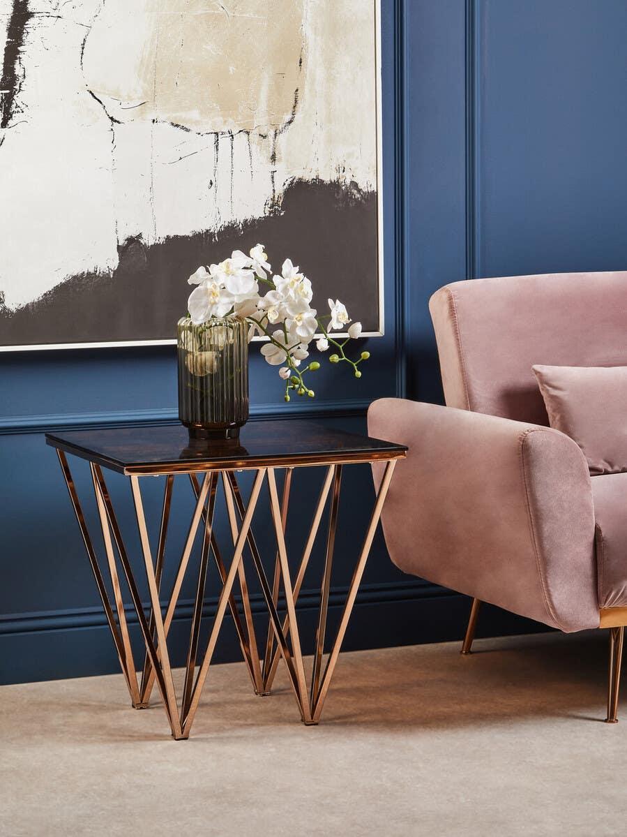 modern gold metal side table with dark top and glass vase beside blush pink armchair
