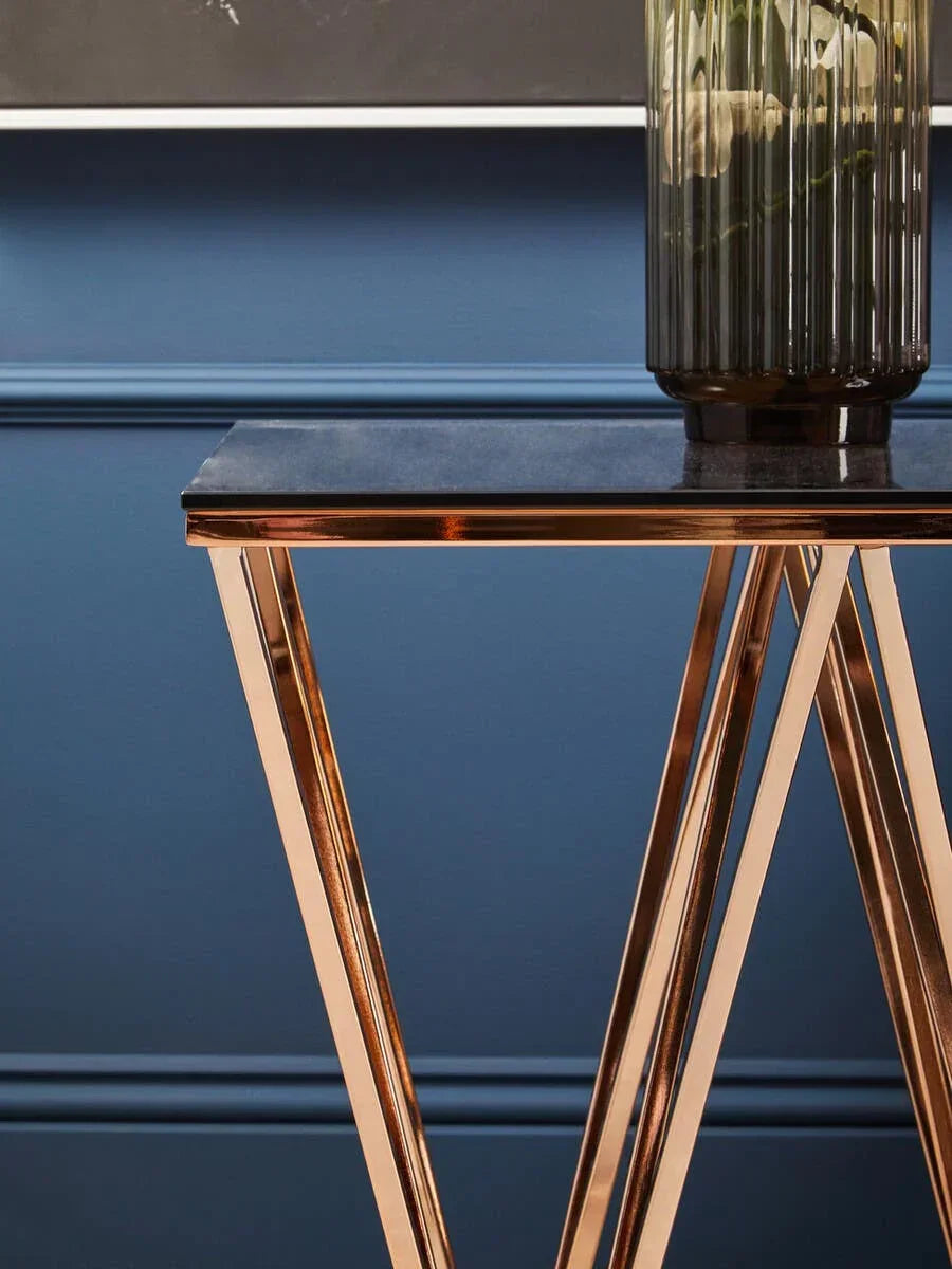 Black marble console table with gold metal legs and glass vase against blue wall